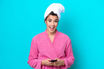 Young Brazilian woman with a bathrobe isolated on blue background surprised and sending a message