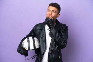 Fototapeta premium Young Brazilian man with a motorcycle helmet isolated on purple background having doubts