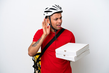 Young Brazilian man with thermal backpack isolated on white background listening to something by putting hand on the ear