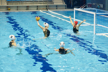 Young female athlete in swimwear throwing ball to player with outstretched arms standing in gate during game or training