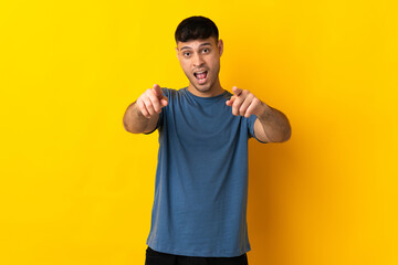 Young Colombian man isolated on yellow background surprised and pointing front