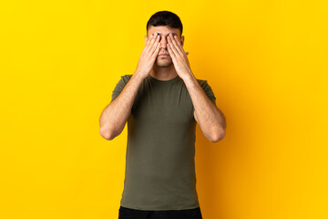Young Colombian man isolated on yellow background covering eyes by hands
