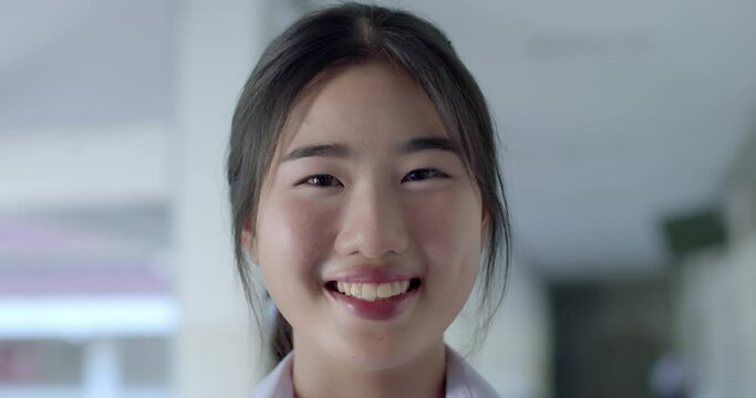 Slow motion scene : A happy smiling Asian high school student girl in white uniform and tie her long hair back with a bow.
