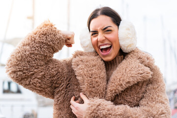 Young woman wearing winter muffs at outdoors doing strong gesture