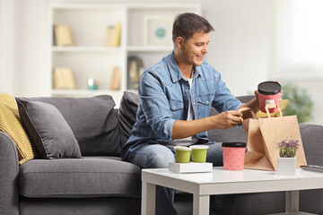 Happy young man sitting on a sofa and opening takeaway food boxes