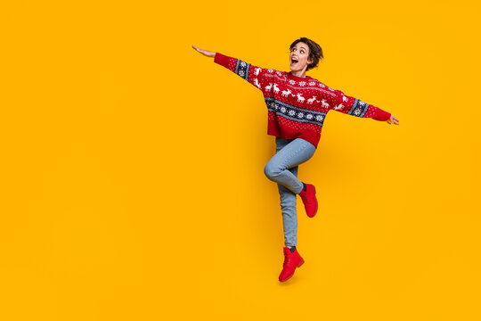 Full body photo of attractive woman wear sweater jumping arms like wings staring at promo empty space isolated on yellow color background