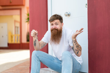 Redhead man with beard holding home keys at outdoors