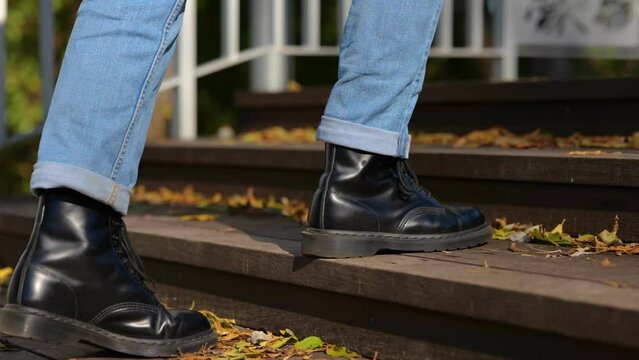 Guy in black boots going up the stairs in the park during sunny day. Leaves on the stairway. Cropped. Concept of autumn walks. Real time concept.