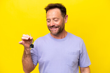 Middle age man holding home keys isolated on yellow background with happy expression
