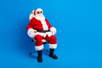 Full length photo of mature pensioner man sit comfy armchair dressed stylish santa claus costume coat isolated on blue color background
