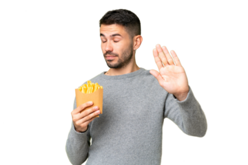 Young caucasian man holding fried chips over isolated chroma key background making stop gesture and disappointed