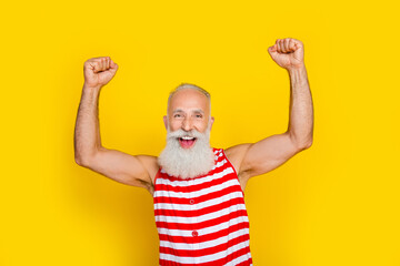 Photo of excited cheerful senior man wear red striped swimsuit shouting yeah rising fists isolated...