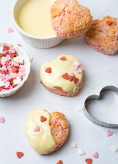 Pink heart shaped cookies drizzled with white icing and sprinkled with little hearts. Preparation for Valentine's Day..