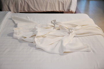 Close-up of two white robes on the bed In the hotel room.White terry cloth bathrobe is a set for the hotel guest to wear the cover when using the spa.Put it on top of your bathing suit or use it while