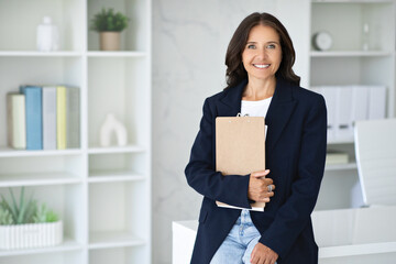 Confident mature woman posing in modern office, holding folder