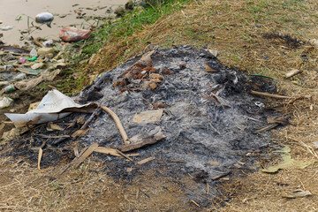 residue from burning garbage on the grass near the river
