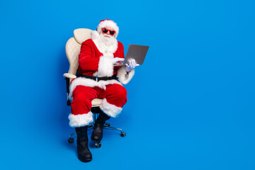 Full length photo of mature pensioner man armchair work netbook dressed stylish santa claus costume...