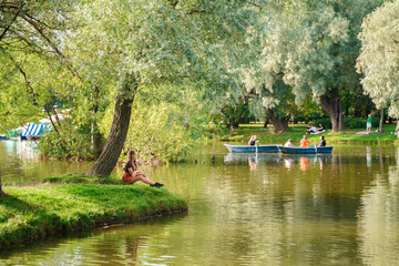 A teenage girl is sitting on the shore of a lake in a summer park,a beautiful landscape