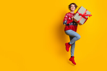 Fototapeta na wymiar Full body photo of satisfied cute woman with stylish hair wear sweater hold present box jumping isolated on yellow color background