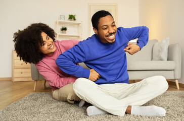 Cheerful black wife bonding with husband through gentle tickles indoor