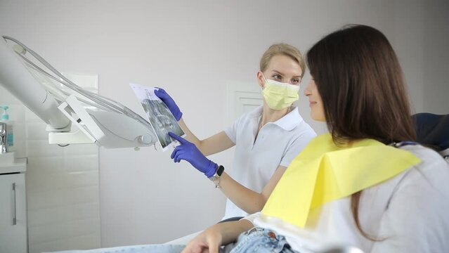 A female dentist shows a photo of an X-ray image of a patient's teeth in a modern dental clinic.
