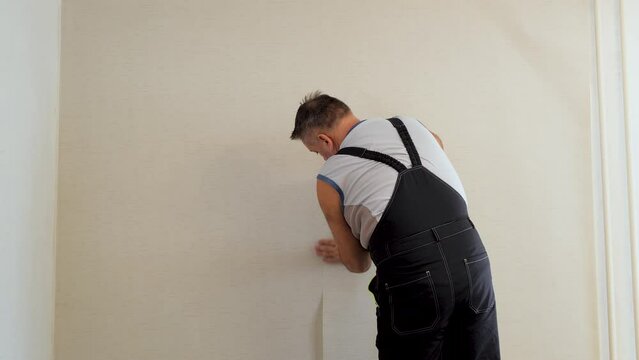 Handyman putting up wallpaper on the wall. Workman glues beige vinyl wallpaper