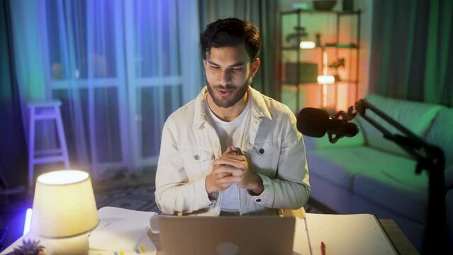 Cheerful young man influencer recording video blog mobile vlog podcast live stream share experience with audience using microphone or having video call conference sitting at desk at home indoors