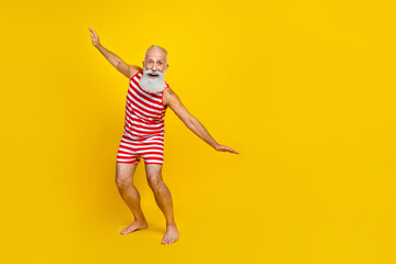 Full length body photo of positive active funky sportive old man surfing ocean waves in summer outfit isolated on yellow color background