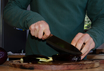 person cooking cutting an eggplant with a knife on a wooden board