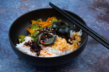 Rice and veggies bowl along with salted egg in a black asian bowl,  chopsticks. Blue textured table. Vegetarian Chinese dish.