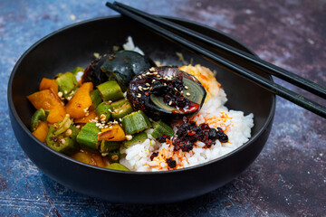 Rice and veggies bowl along with salted egg in a black asian bowl,  chopsticks. Blue textured table. Vegetarian Chinese dish.