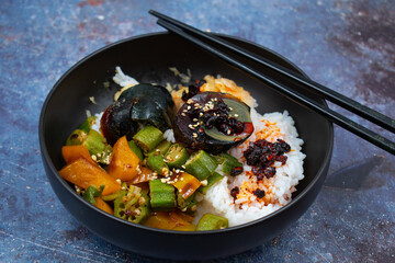 Rice and veggies bowl along with salted egg in a black asian bowl,  chopsticks. Blue textured table. Vegetarian Chinese dish.