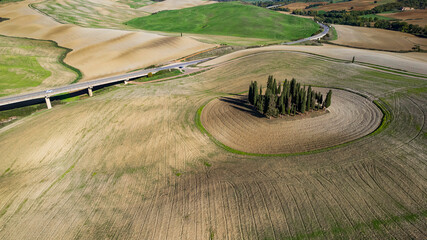Naklejka premium Italy landscape. Amazing Tuscany scenery. Typical countryside with vast fields of Val d'Orcia famous beautiful valley. Aerial drone shot of circle cypresses trees, high angle view