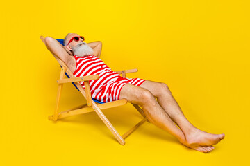 Full length photo of relaxing funky senior man wear red striped lying deck chair hands behind head empty space isolated yellow color background
