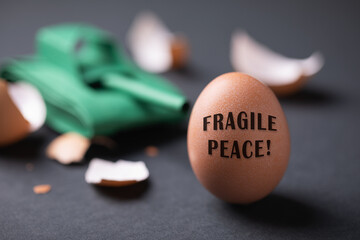 Toy paper tank, broken and whole egg on a dark background, concept on the theme of instability in the world