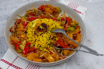 Vegan yellow rice pilaf with pepper curry  in  white bowl, fork and spoon