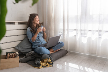Happy young freelance business woman sitting on the floor at home working on a laptop computer
