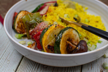 Vegan vegetable skewers with yellow rice in a white bowl. Stylish table setting.