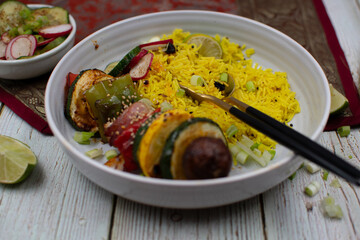 Vegan vegetable skewers with yellow rice in a white bowl. Stylish table setting.