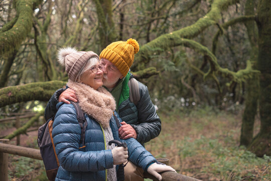 elderly family couple during the hike in La Gomera national park exchange cuddles and kisses. Active elderly man and woman hiking in a green mountain forest enjoying nature and healthy lifestyle