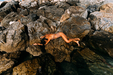 A beautiful young, sensual woman in a swimsuit is lying on the rocks by the sea.