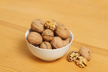 white bbowl of walnuts on wooden surface
