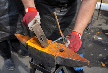 Blacksmith hands holding forceps and a hammer forging a metal billet nail on an anvil