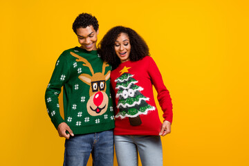 Photo of excited positive guy girl dressed christmas ugly print pullovers showing outfits empty space isolated yellow color background