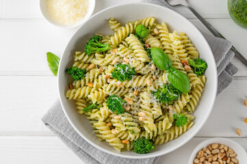 Vegetarian pasta with pesto sauce, broccoli, parmesan cheese and pine nuts on a white wooden background. Healthy food.