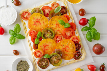 Raw tomatoes pie or galette from puff pastry and cheese filling on a white wooden background. Vegetarian healthy food. Selective focus.