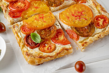 Tomatoes pie or galette from puff pastry and cheese filling on a white wooden background. Vegetarian healthy food. Selective focus.