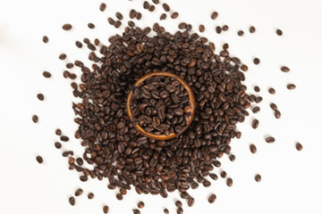 Many coffee beans overflowing from a wooden cup scattered on a white background.
