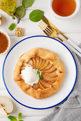 Autumn galette with pear, ice cream, walnuts, caramel sauce and cinnamon on a white wooden background.