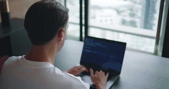 Programming professional in action, male IT programmer meticulously crafting lines of code on his laptop. Digital Workspace, Man Programming on Laptop computer, Rear View in Office Setting
